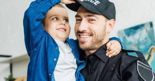 A police officer and his son smiling together as his son plays with his hat.