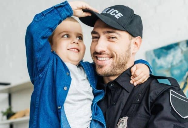 A police officer and his son smiling together as his son plays with his hat.
