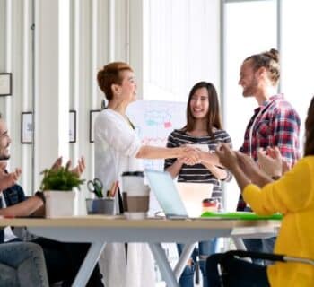 A office conference room full of coworkers congratulating a fellow coworker for an award.