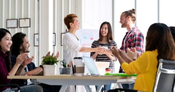 A office conference room full of coworkers congratulating a fellow coworker for an award.