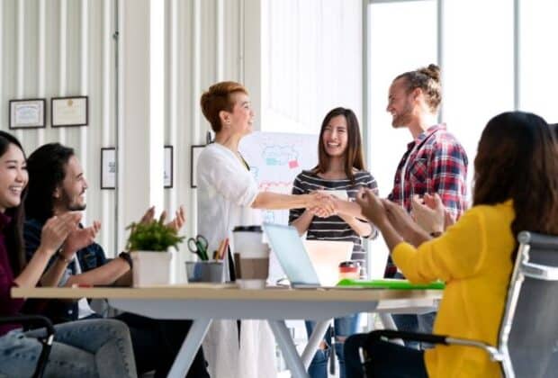 A office conference room full of coworkers congratulating a fellow coworker for an award.
