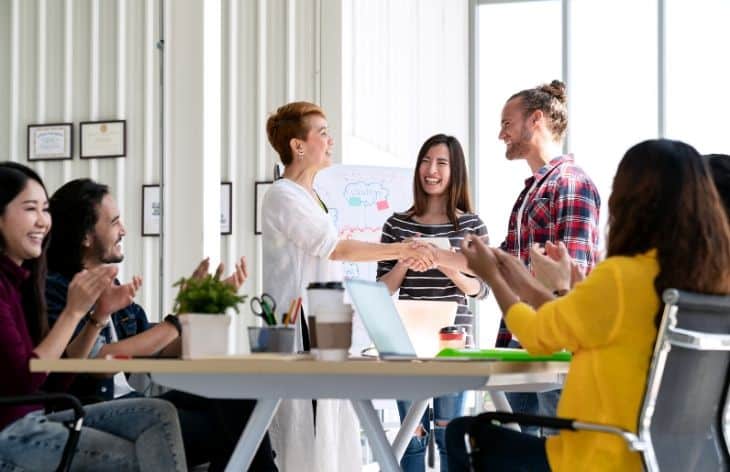 A office conference room full of coworkers congratulating a fellow coworker for an award.